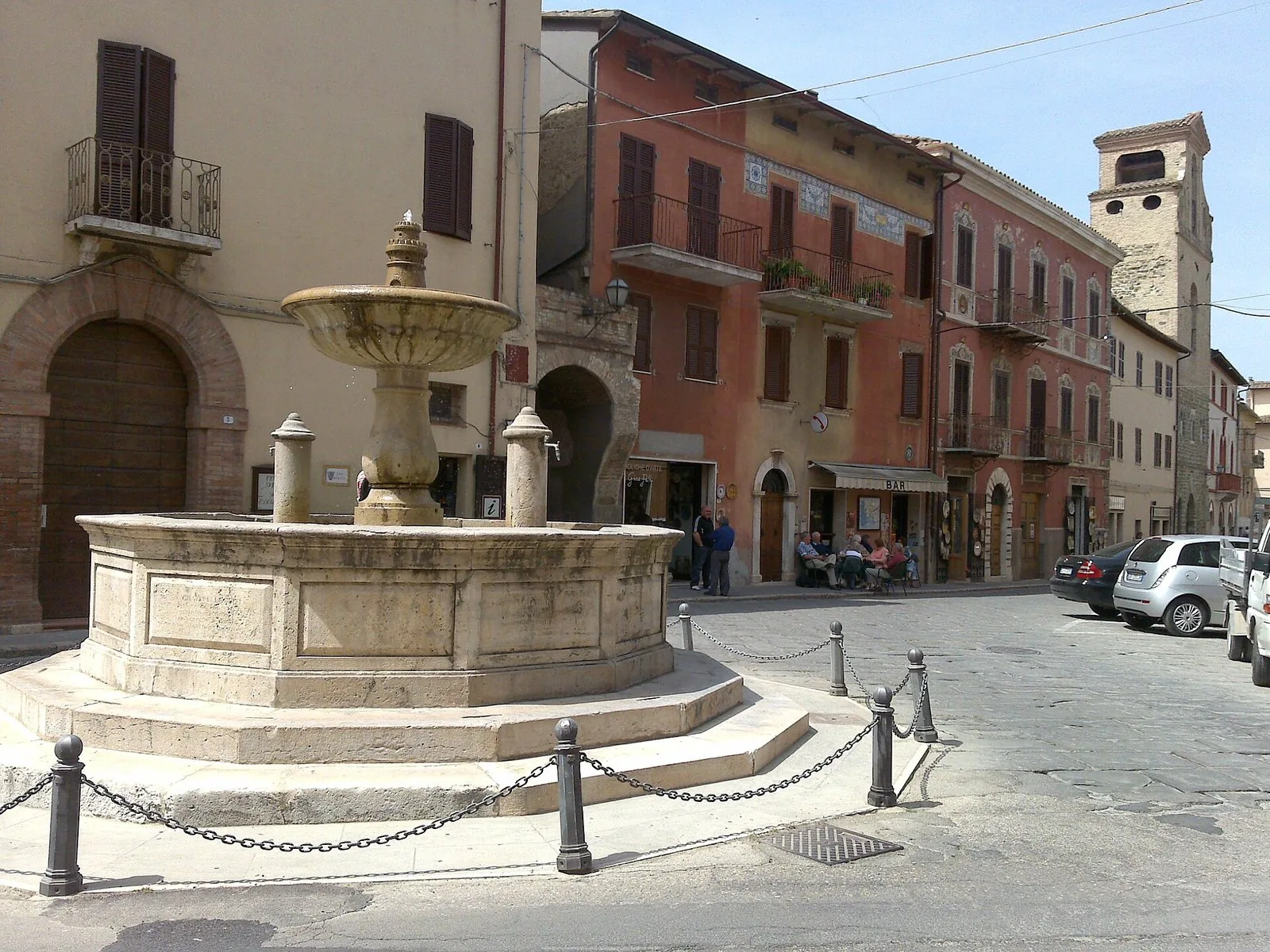 La fontana in pietra di Piazza dei Consoli nel centro storico di Deruta, con case color terracotta e il campanile